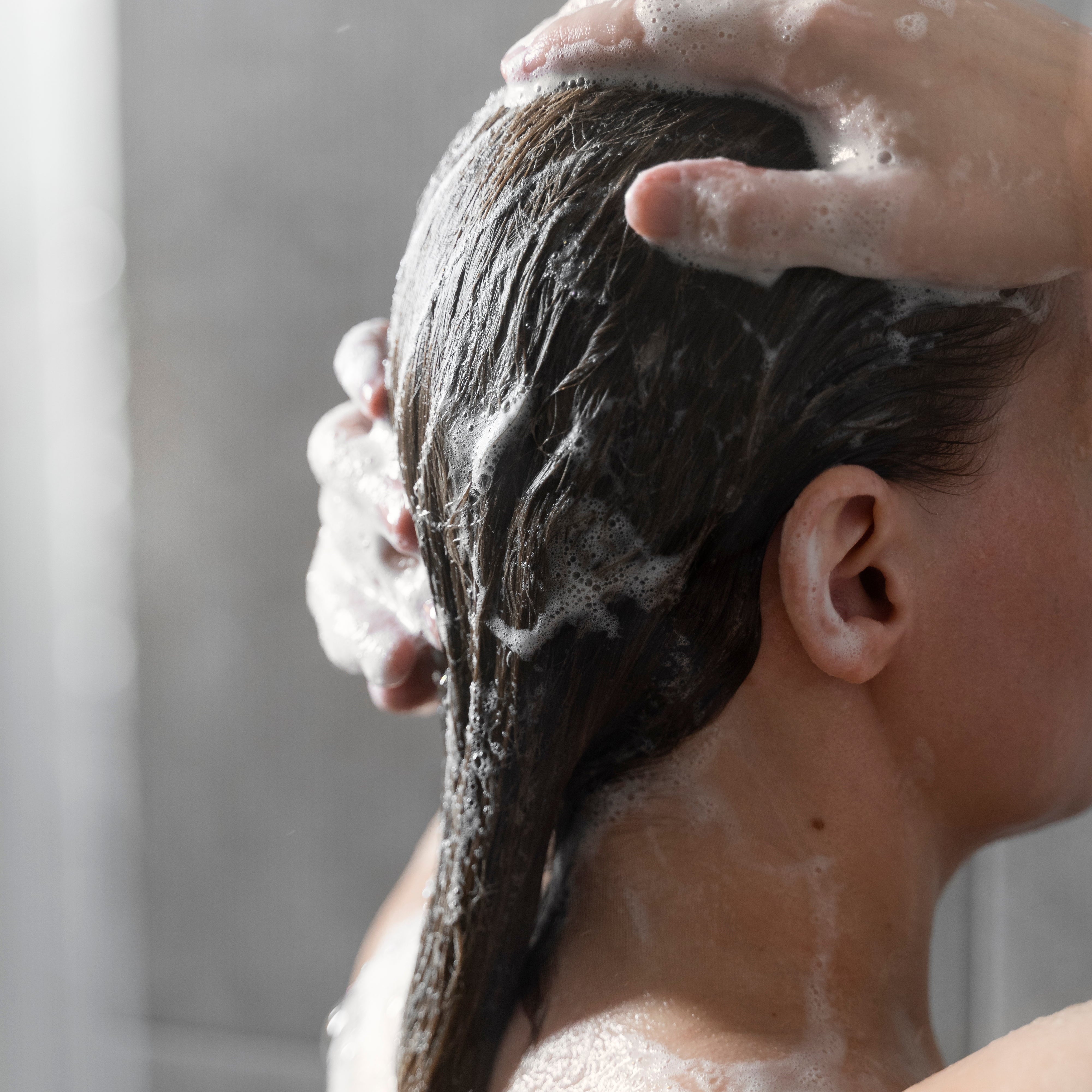 Woman massaging foaming shampoo into her hair in the shower, a gentle scalp care routine with provitamin B5.